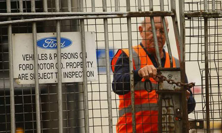 A security guard locks a gate after workers left the Ford Transit Assembly Plant in Southampton, England after being told that the site will close. (Chris Ison/PA/Associated Press)