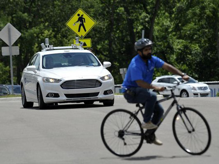 A Ford Fusion autonomous car waits for a cyclist to turn Wednesday at Mcity.