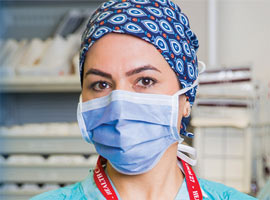 A female Unifor member and nurse wearing a surgical mask and a patterned blue scrub cap, looking at the camera in a hospital setting.