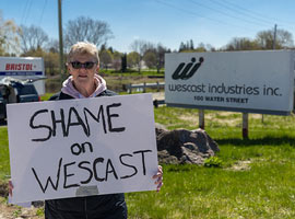 Woman standing outside holding a ‘Shame on Wescast’ sign 